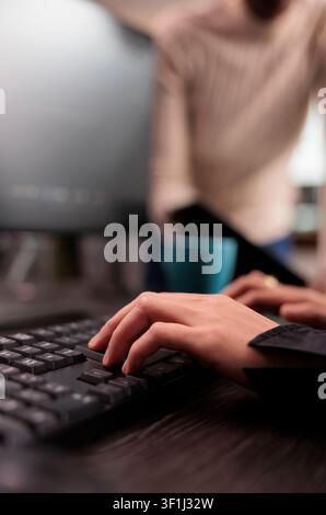 Programming team types machine learning code at a computer desk in an IT security agency, working together on databases, HTML script and software tasks. Stock Photo