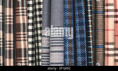 Close-up of various plaid fabric swatches. Colors range from deep blue to red and beige. Patterns include houndstooth, check, and striped designs. Tex Stock Photo