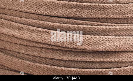 Close-up of tightly twisted brown fabric cord, used as  solid background. textured surface reveals fine woven fibers. layering creates smooth, curved Stock Photo