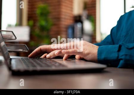 Focused detail of hands of startup employee typing on digital device, updating company information at office desk, caucasian person seated at table, using laptop to input business project details. Stock Photo