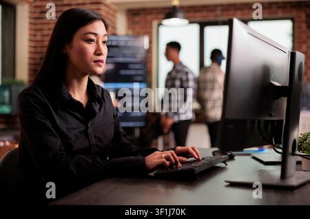 Asian programmer reviewing HTML script on terminal window at an IT office desk, using screens, scripts and cloud computing tools for software engineering workflow. Stock Photo