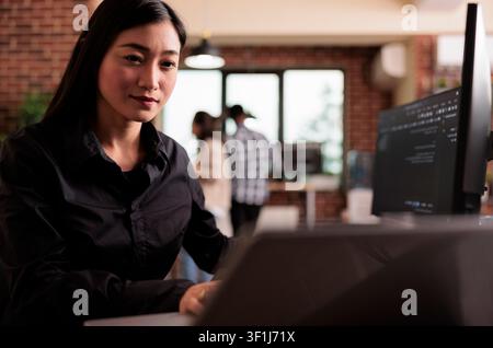 Asian freelance coder analyzes compiling HTML code on a monitor, working on interface development and programming tasks in an agency. Stock Photo
