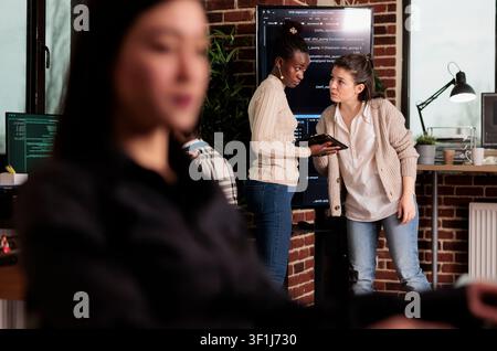 Two software developers inspect source code on a wall monitor, checking errors and reviewing programming work inside an IT agency. Stock Photo
