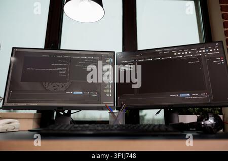 Multiple empty office monitors display programming code and algorithm data, showing software development work inside an IT agency. Stock Photo