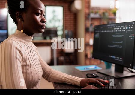 African American programmer sits at a computer typing big data code, developing HTML script and artificial intelligence algorithms in a programming agency. Stock Photo