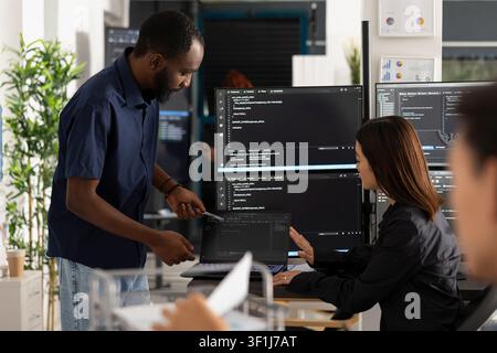 Diverse programmers work together in office, reviewing HTML code on multiple screens. Male and female developers plan digital solutions, improving app functionality through collaboration and innovation Stock Photo