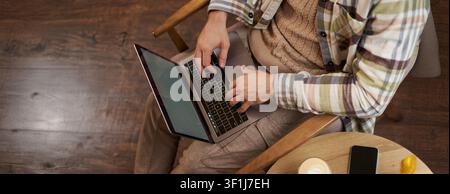 Upper angle cropped shot of male hands, man sitting in cafe with cup of coffee and working on laptop, typing on keyboard, has a phone on the table Stock Photo