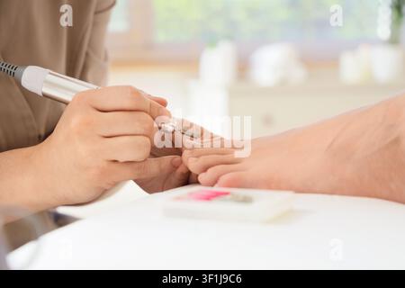 Pedicurist performing a professional electric pedicure on a clients foot at a modern beauty salon, the technician uses a specialized electric drill to Stock Photo