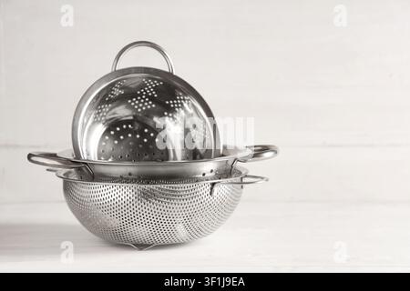 Stack of three stainless steel colanders and strainers for kitchen and cooking on a white wooden background, These kitchen utensils are used for drain Stock Photo