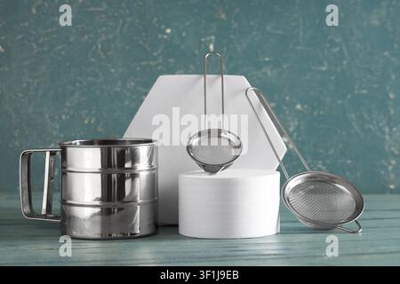 Stainless steel flour sifter and two mesh strainers for baking and cooking on a textured blue background, White geometric props elevate the kitchen to Stock Photo