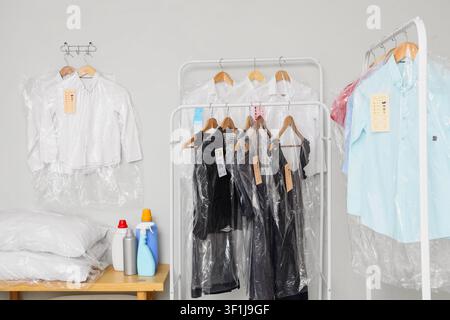 Cleaned clothes in plastic bags hanging on racks and wall hooks at a professional laundry service Stock Photo
