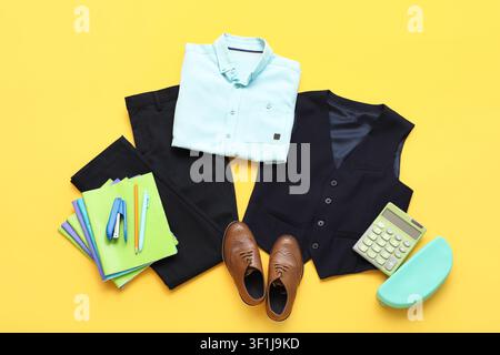 School uniform with light blue shirt, black pants, vest, brown shoes, and School supplies on yellow background Stock Photo