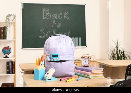 Back to School classroom scene with a purple backpack, books, and School supplies on a wooden desk Stock Photo