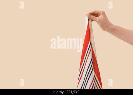 Hand holding a striped fabric with red, white, and black lines, textile and fashion concept, against a beige background Stock Photo