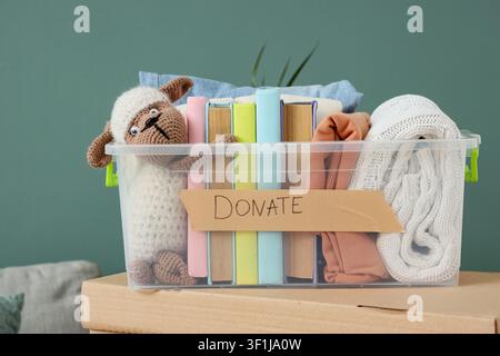 Clear plastic donation box filled with books, clothes, and a stuffed animal on cardboard boxes, charity and giving Stock Photo