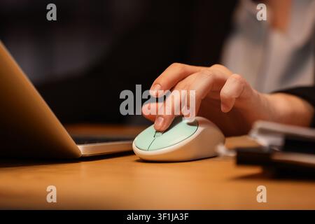 Persons hand using a mint green computer mouse on a wooden desk next to a laptop, close-up view Stock Photo
