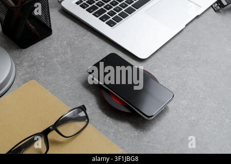 Modern mobile phone, wireless charger pad, laptop and notebook on grunge background Stock Photo