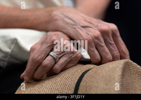 Close-up of an older person’s hands resting on a straw hat. Stock Photo