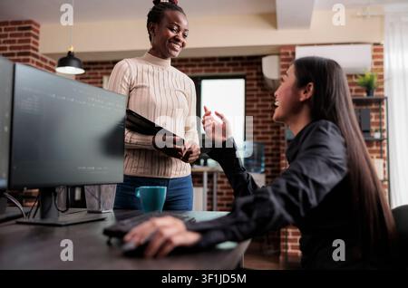 Tech coworkers laughing during computer break presents a row-specific commercial moment, illustrating Christmas celebration, pet companionship and family warmth inside a technology office. Stock Photo