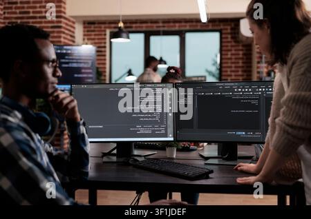 Multiethnic cybersecurity team members work at an agency desk writing cloud database processing algorithms and building a functional encryption system. Stock Photo