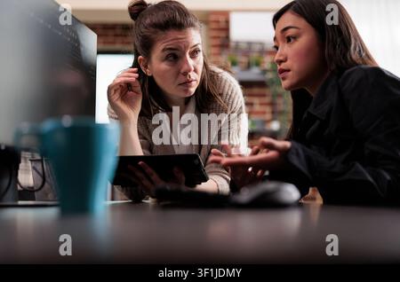Blockchain developer troubleshooting database security showing unsure asian programming expert asking colleague about generated bug report file. Stock Photo