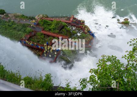 A high-angle horizontal shot looking down at crowds of tourists wearing yellow and blue rain ponchos on wooden observation platforms and walkways at t Stock Photo