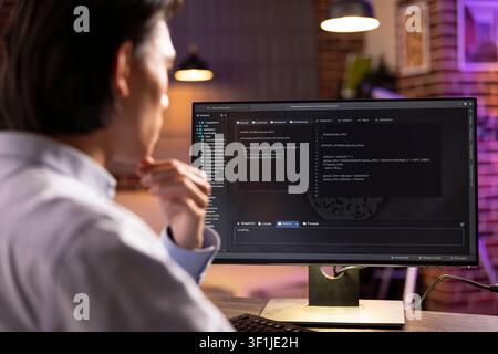 Closeup of software developer looking at desktop pc displaying lines of code. Young man reviews programming scripts, checks for errors and ensures smooth website functionality for client projects. Stock Photo