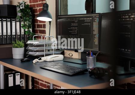 Empty office contains multiple computer displays with programming data, software information and integrated algorithms for secure technical work. Stock Photo