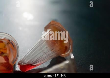 Closeup of an empty plastic jelly cup with leftover red jelly on a dark surface highlighting disposable food packaging snack container and everyday co Stock Photo