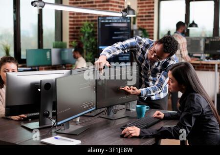 Cybersecurity coworker points to high processing power usage on a data grid screen while engineers investigate a cloud technology issue. Stock Photo