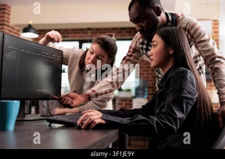 Multiethnic cybersecurity team works on encrypting a mainframe database and developing firewall protection after a system breach, inside a software security workflow. Stock Photo