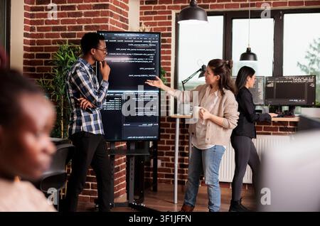 Diverse software developers collaborate on an IT project, coding company network systems and reviewing technical updates together. Stock Photo