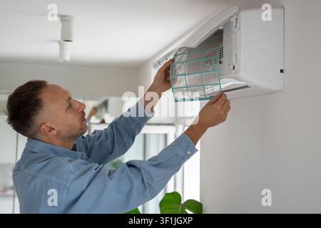 Man cleaning air conditioner at home, taking out dirty dusty filter from cooling system to replace. Stock Photo