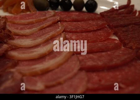 Assorted smoked sausages and thin ham slices decorated with artistic carved carrot flowers and olives on a white plate, gourmet charcuterie platter Stock Photo