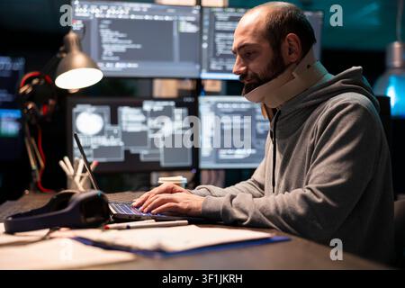 White man recovering from neck injury works late in office, creating software and debugging encrypted programs. Caucasian male programmer with cervical collar, writing coding scripts on laptop. Stock Photo