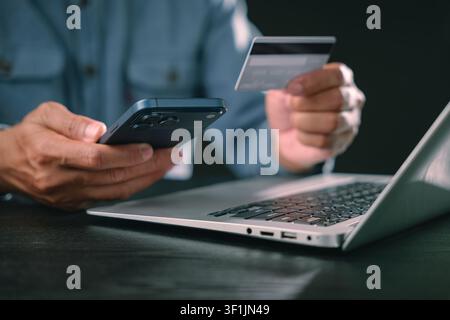 Man uses smartphone, digital, display, cyber, security, online, shopping, protection while paying with credit card on laptop, completing safe mobile p Stock Photo