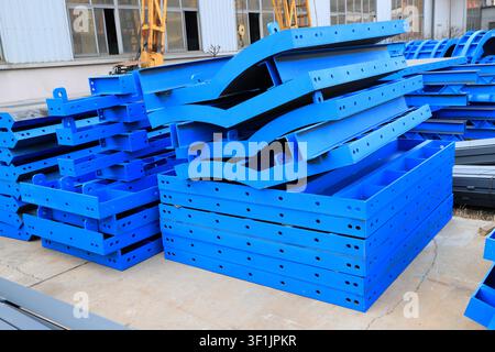 The image shows neatly stacked blue curved steel formwork in a factory area. The metal plates are covered with connecting holes and lifting lugs, whic Stock Photo