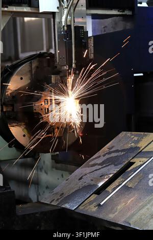 The image shows CNC laser cutting equipment precisely cutting perforated metal profiles, with high-temperature sparks bursting and splashing. The prec Stock Photo