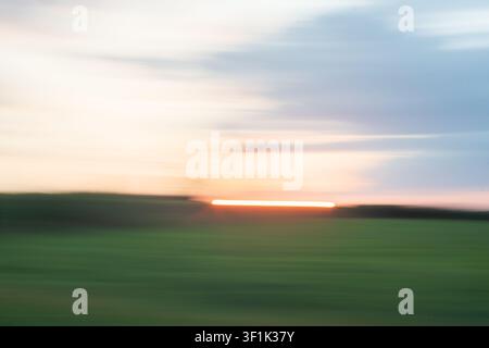 Abstract intentional camera motion blur effect with flowing light in sunset colours of blue and orange over a green field.. Stock Photo