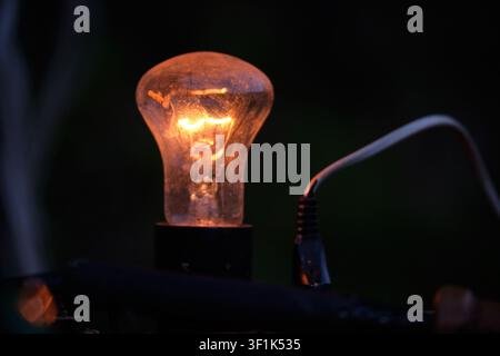 A close-up shot of a single vintage incandescent light bulb glowing warmly against a dark, moody background, emphasizing energy and inspiration. Stock Photo