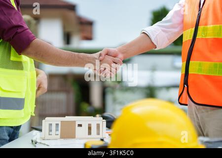 Construction workers shaking hands over architectural model for business agreement Stock Photo