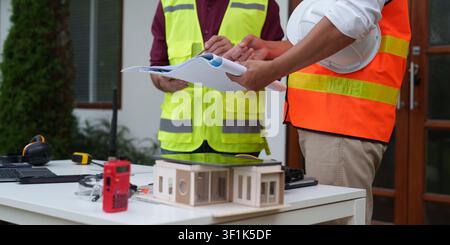 Cropped shot of architects reviewing blueprints over house model at construction site Stock Photo