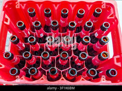 DENIA, SPAIN - August 10, 2025. Empty bottles collected in a red plastic crate sit on a table after a social event. The gathering featured drinks and Stock Photo