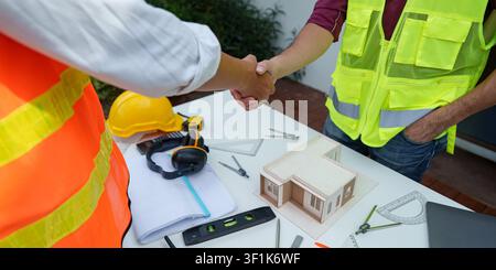 Cropped shot of construction workers shaking hands over house model for real estate development agreement Stock Photo
