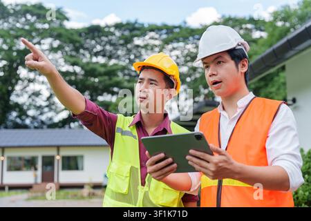 Asian construction engineers with tablet pointing and discussing building plan at site Stock Photo