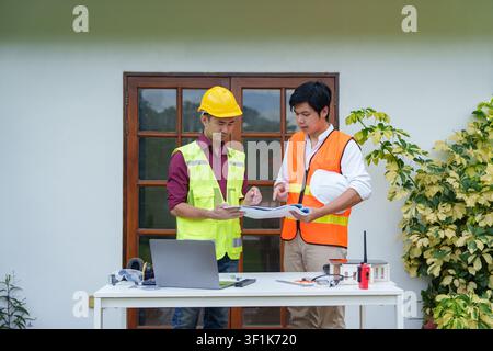 Asian construction engineers reviewing blueprints at outdoor workspace Stock Photo