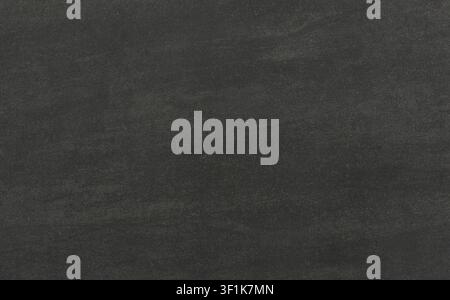 A full-frame background of a dark charcoal grey slate or basalt stone showing a subtle brushed texture with natural organic variations. Stock Photo