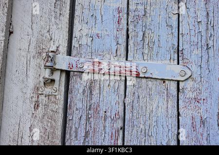 Weathered wooden door with peeling paint and rusted metal latch. Metal hardware shows age, decay, and quiet resilience. Peeling paint reveals the wood Stock Photo