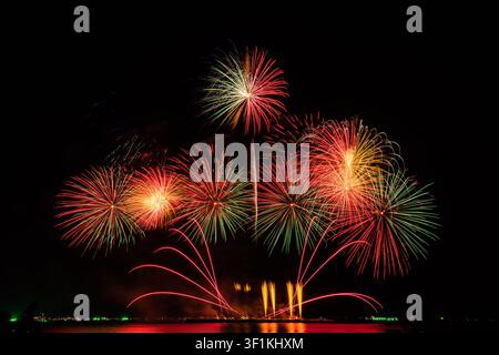 Vibrant pyrotechnic patterns explode in the night sky creating brilliant light trails and reflections on the dark water surface. Stock Photo