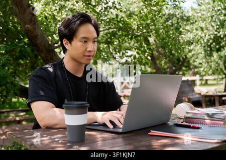 Freelancing under green trees, this young asian man enjoys remote work and coffee Stock Photo
